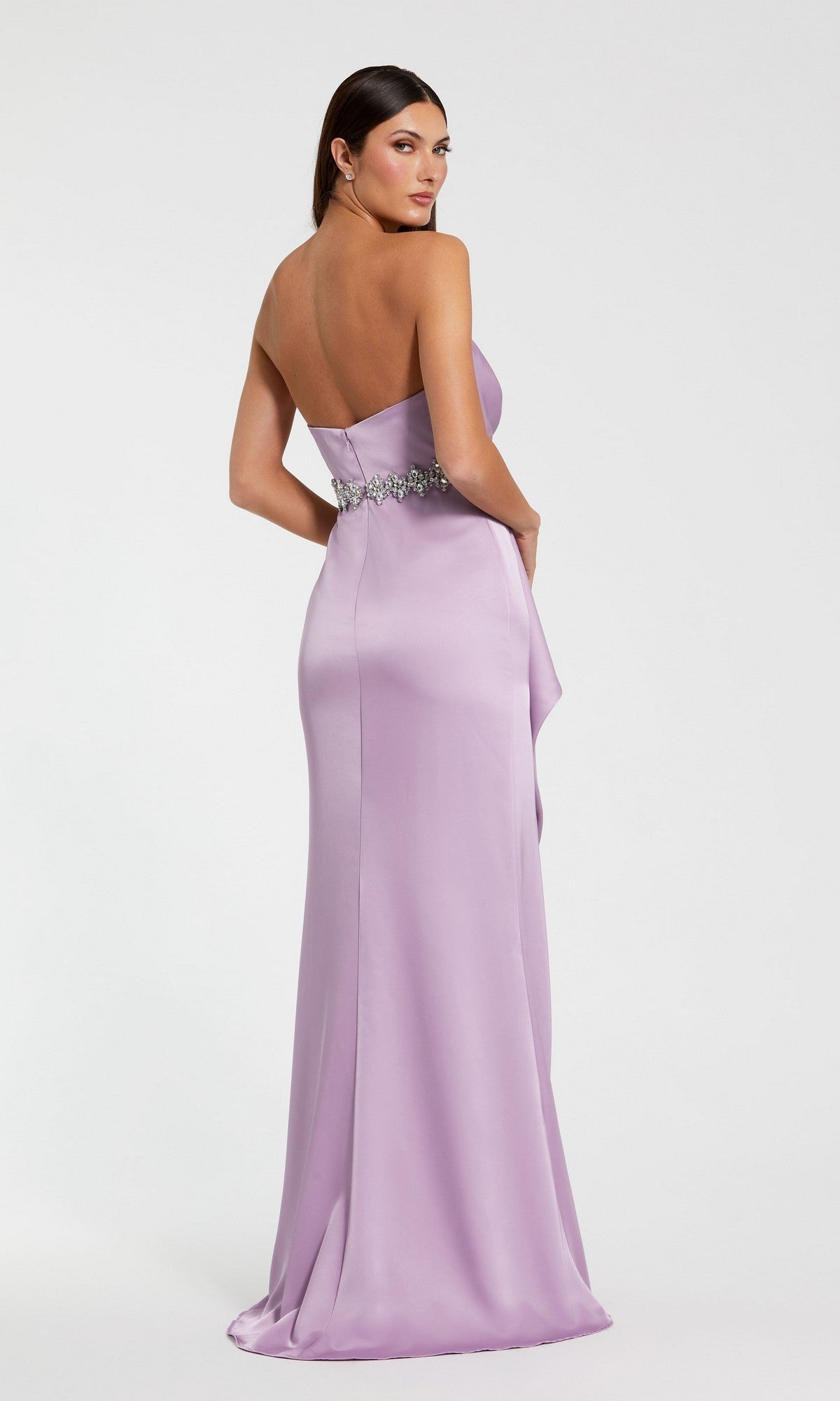 A woman models the Mac Duggal 44133 long formal dress—a strapless lilac satin gown with an embellished belt—as she stands, looking over her shoulder against a plain background.